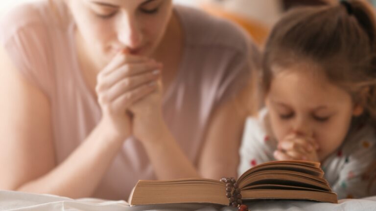 Mom and daughter praying together with an open Bible, fostering faith and connection.