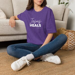Woman wearing purple Jesus Heals T-shirt sitting on the floor.